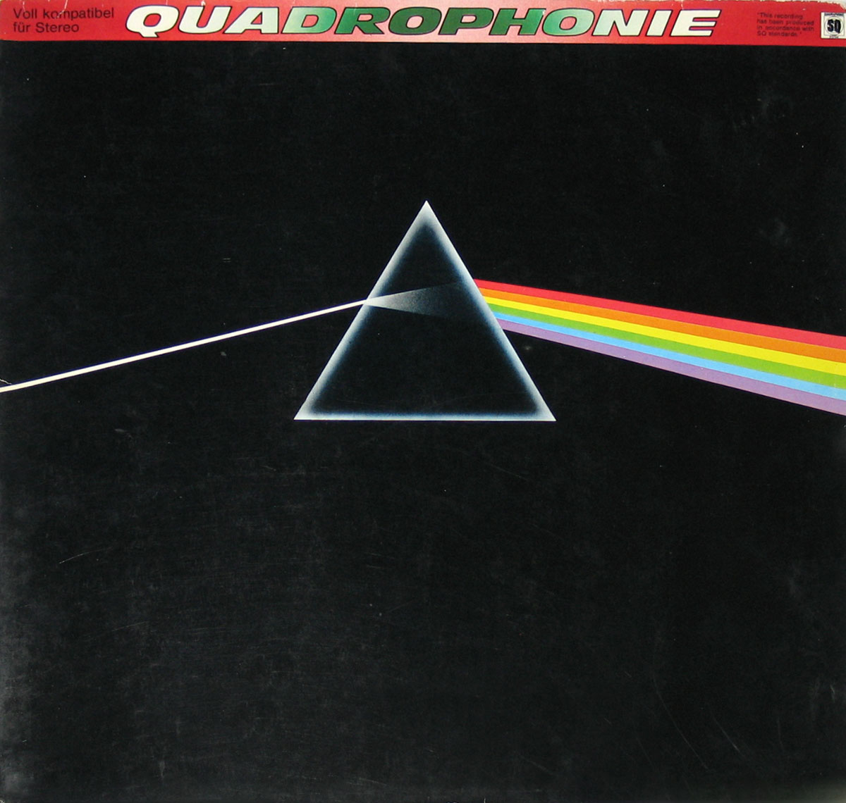 Album cover of Pink Floyd’s The Dark Side of the Moon quadraphonic edition. The cover features a black background with a white light beam entering from the left, hitting a central triangular prism, and dispersing into a rainbow spectrum that exits to the right. The top section has the text “QUADROPHONIE” in bold, with additional German text indicating compatibility with stereo systems.
